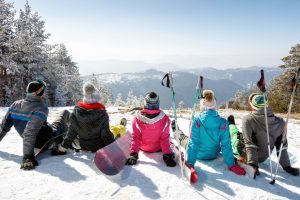 Group of skiers sitting on snow and looking beautiful landscape, back view