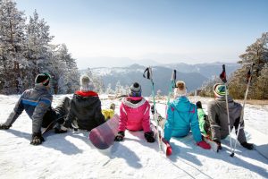 Group of skiers sitting on snow and looking beautiful landscape, back view