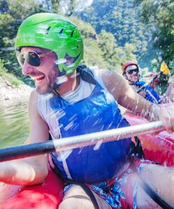 A happy laughing male in a canoe is being sprayed with water by his friends from another boat.