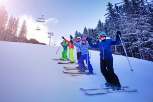 Ski school group of kids stand on the slope in a line and happy lifting hands