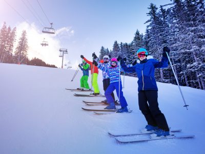 Ski school group of kids stand on the slope in a line and happy lifting hands