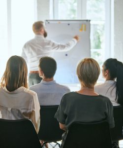 Female speaker giving a talk at business meeting. Audience in conference hall. Concept of conference, training, planning, learning, coaching, business. Panoramic composition suitable for banners.