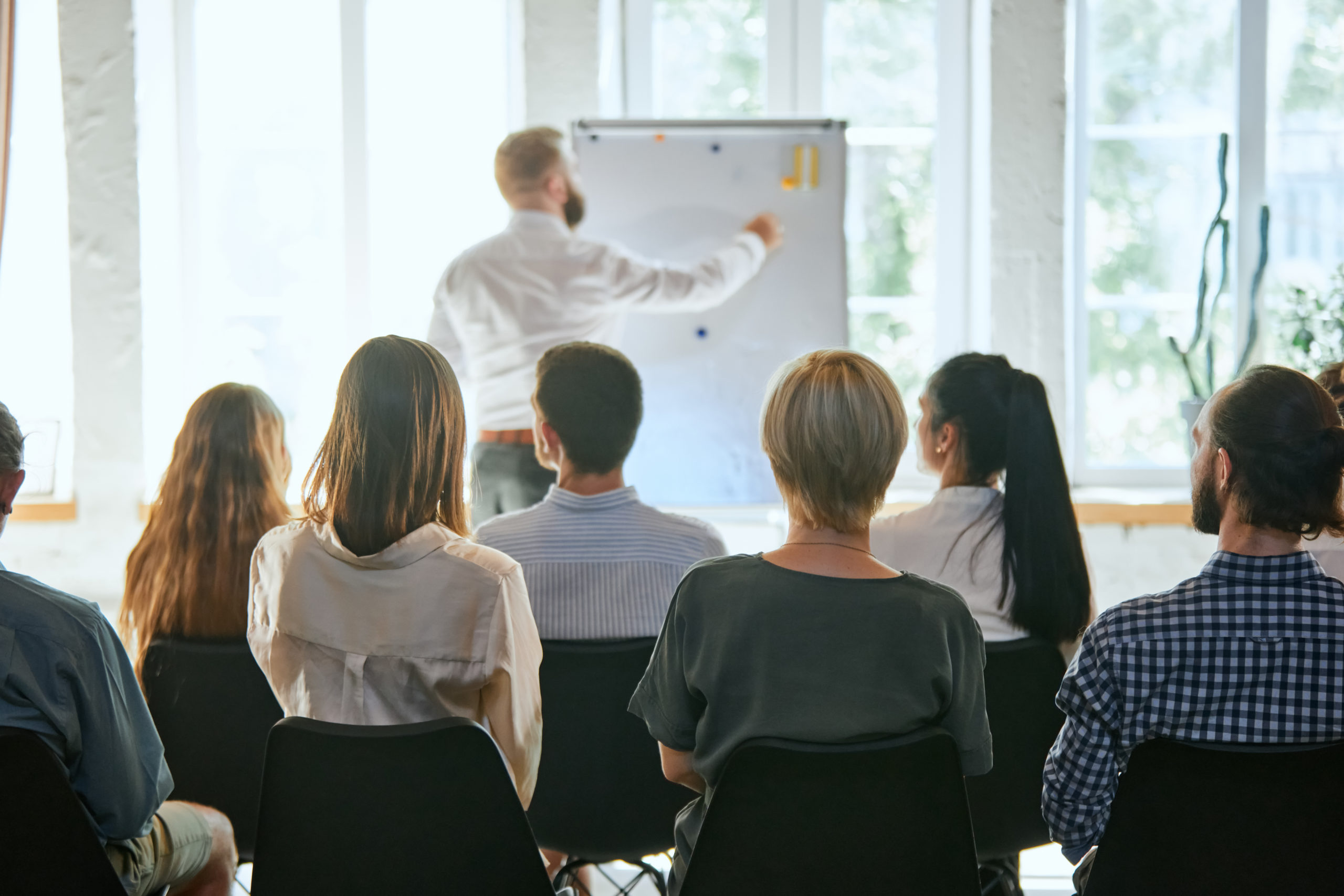 Female speaker giving a talk at business meeting. Audience in conference hall. Concept of conference, training, planning, learning, coaching, business. Panoramic composition suitable for banners.