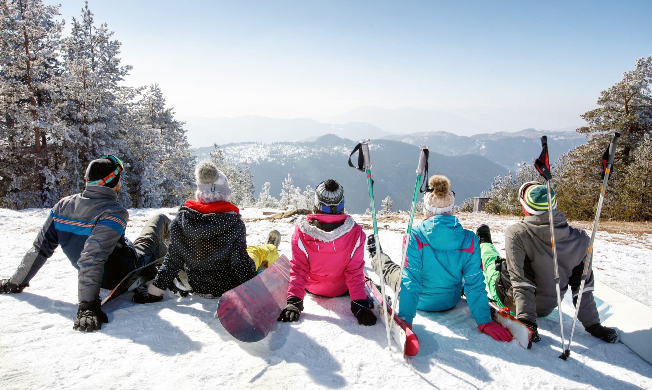 Group of skiers sitting on snow and looking beautiful landscape, back view
